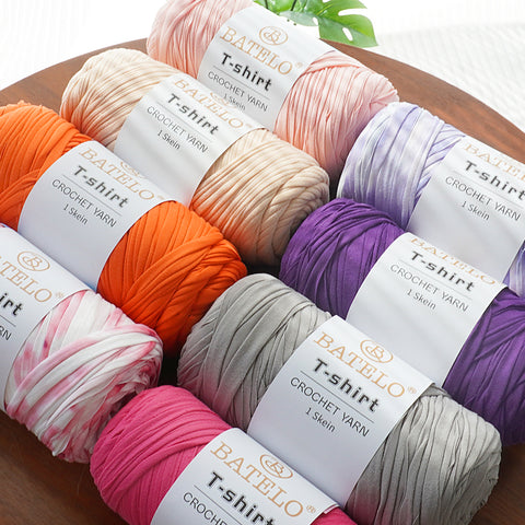 Assorted BATELO T-shirt yarn skeins in orange, pink, purple, cream, and gray on a wooden table