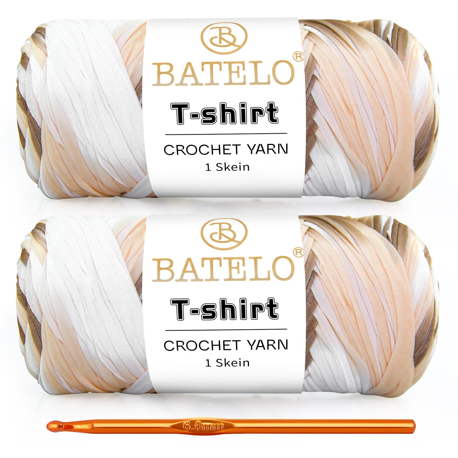 Two cream, tan, and black variegated BATELO T-shirt yarn skeins with a gold crochet hook on a white background