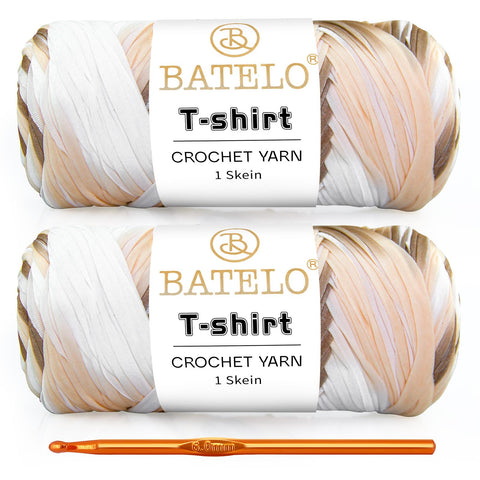 Two cream, tan, and black variegated BATELO T-shirt yarn skeins with a gold crochet hook on a white background