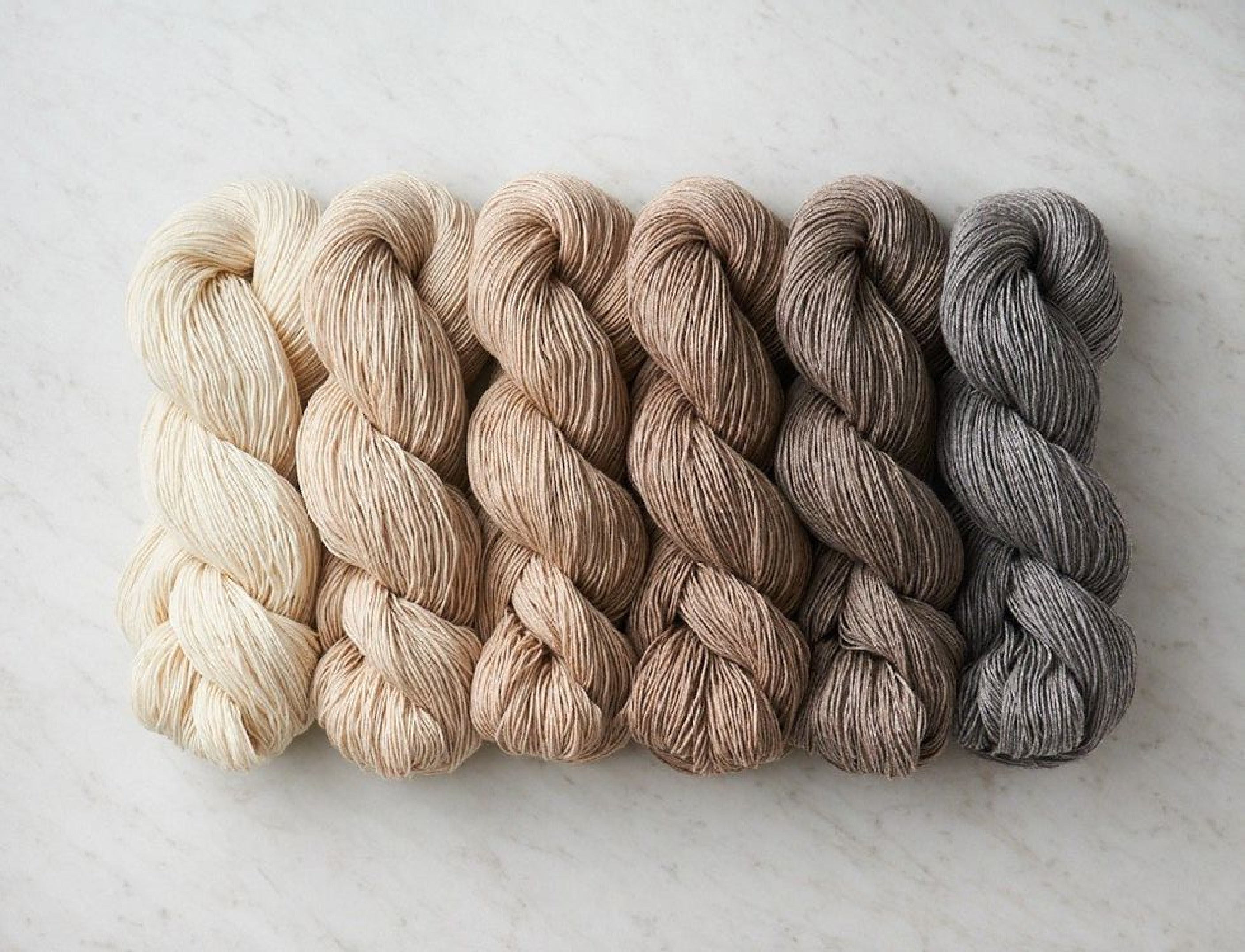 Neutral yarn color samples arranged from cream and beige to brown and gray on a pale background