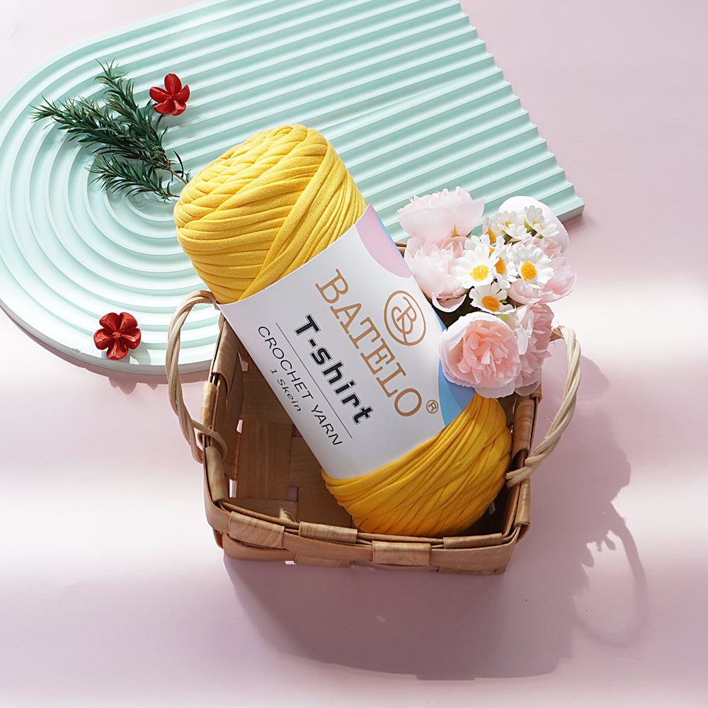 Yellow BATELO T-shirt yarn skein in a wicker basket with flowers on a pink tabletop