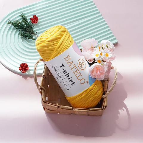 Yellow BATELO T-shirt yarn skein in a wicker basket with flowers on a pink tabletop