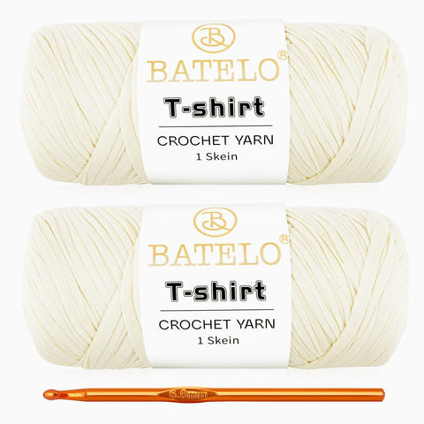 Two ivory BATELO T-shirt yarn skeins with a gold crochet hook on a white background