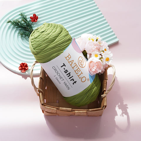 Light Green BATELO T-shirt yarn skein in a wicker basket with flowers on a pink tabletop