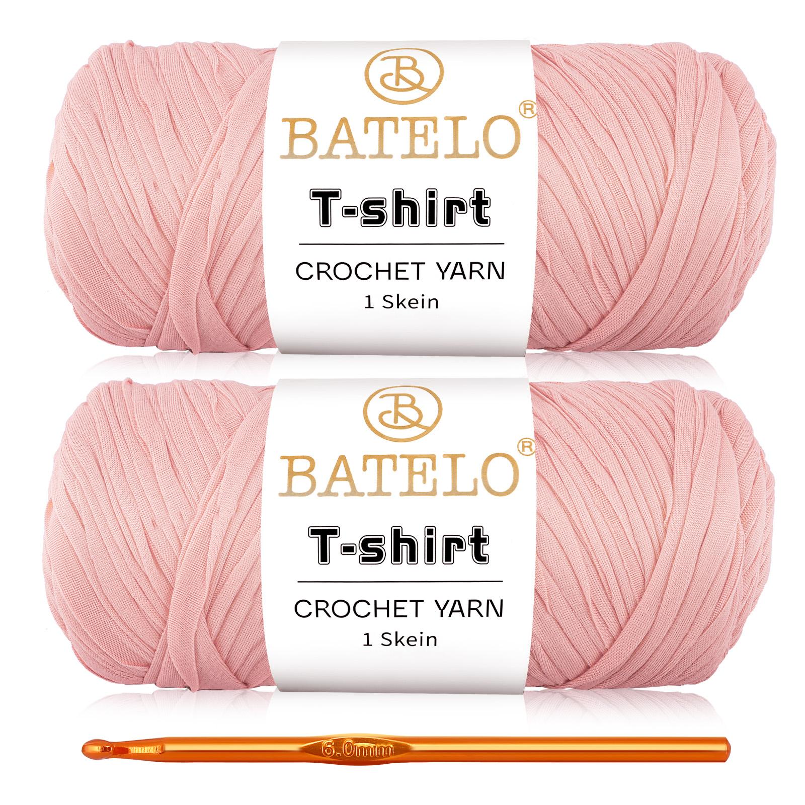 Two light pink BATELO T-shirt yarn skeins with a gold crochet hook on a white background