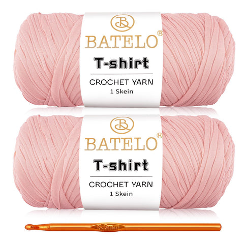 Two light pink BATELO T-shirt yarn skeins with a gold crochet hook on a white background