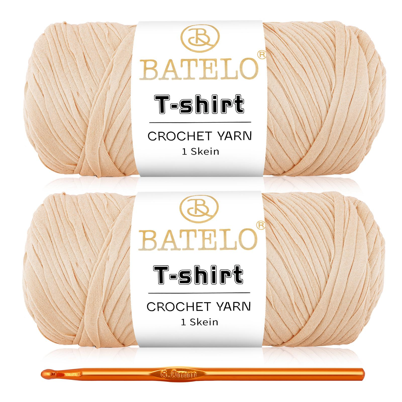 Two peach beige BATELO T-shirt yarn skeins with a gold crochet hook on a white background