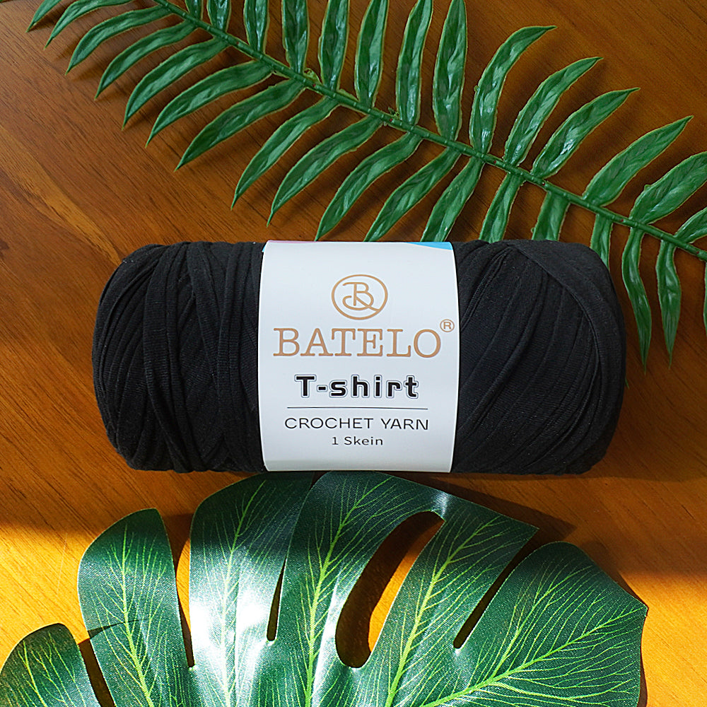 Single black BATELO T-shirt crochet yarn skein on a wooden table with green leaves