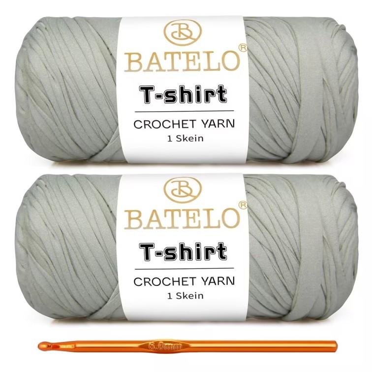 Two pale gray BATELO T-shirt yarn skeins with a gold crochet hook on a white background