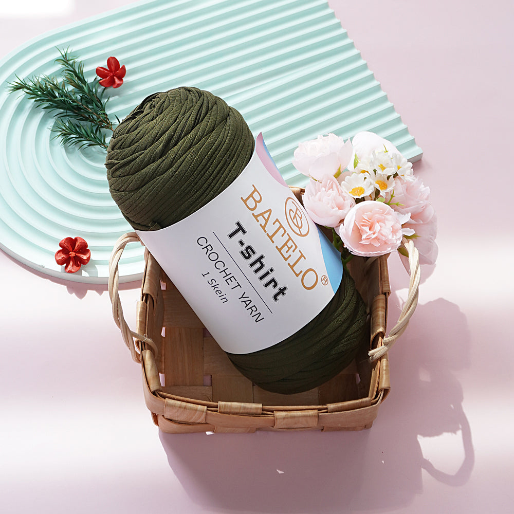 Dark Olive BATELO T-shirt yarn skein in a wicker basket with flowers on a pink tabletop
