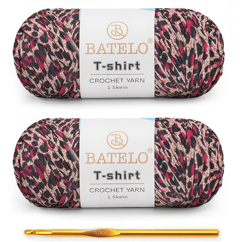 Two black, pink, and cream variegated BATELO T-shirt yarn skeins with a gold crochet hook on a white background