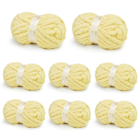 Eight pale yellow BATELO chunky chenille yarn skeins arranged on a white background