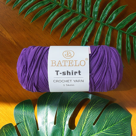 Single purple BATELO T-shirt crochet yarn skein on a wooden table with green leaves