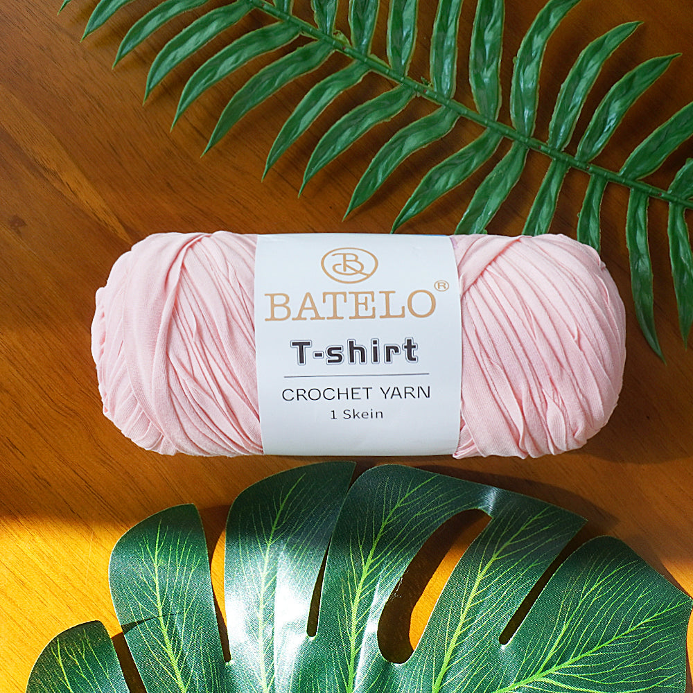 Single light pink BATELO T-shirt crochet yarn skein on a wooden table with green leaves