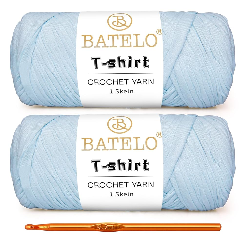 Two light blue BATELO T-shirt yarn skeins with a gold crochet hook on a white background