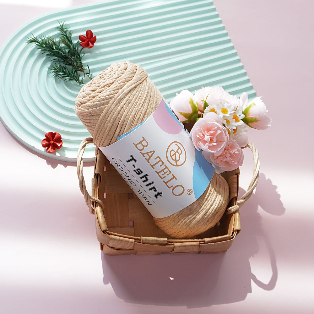 Beige BATELO T-shirt yarn skein in a wicker basket with pink flowers on a pale pink tabletop