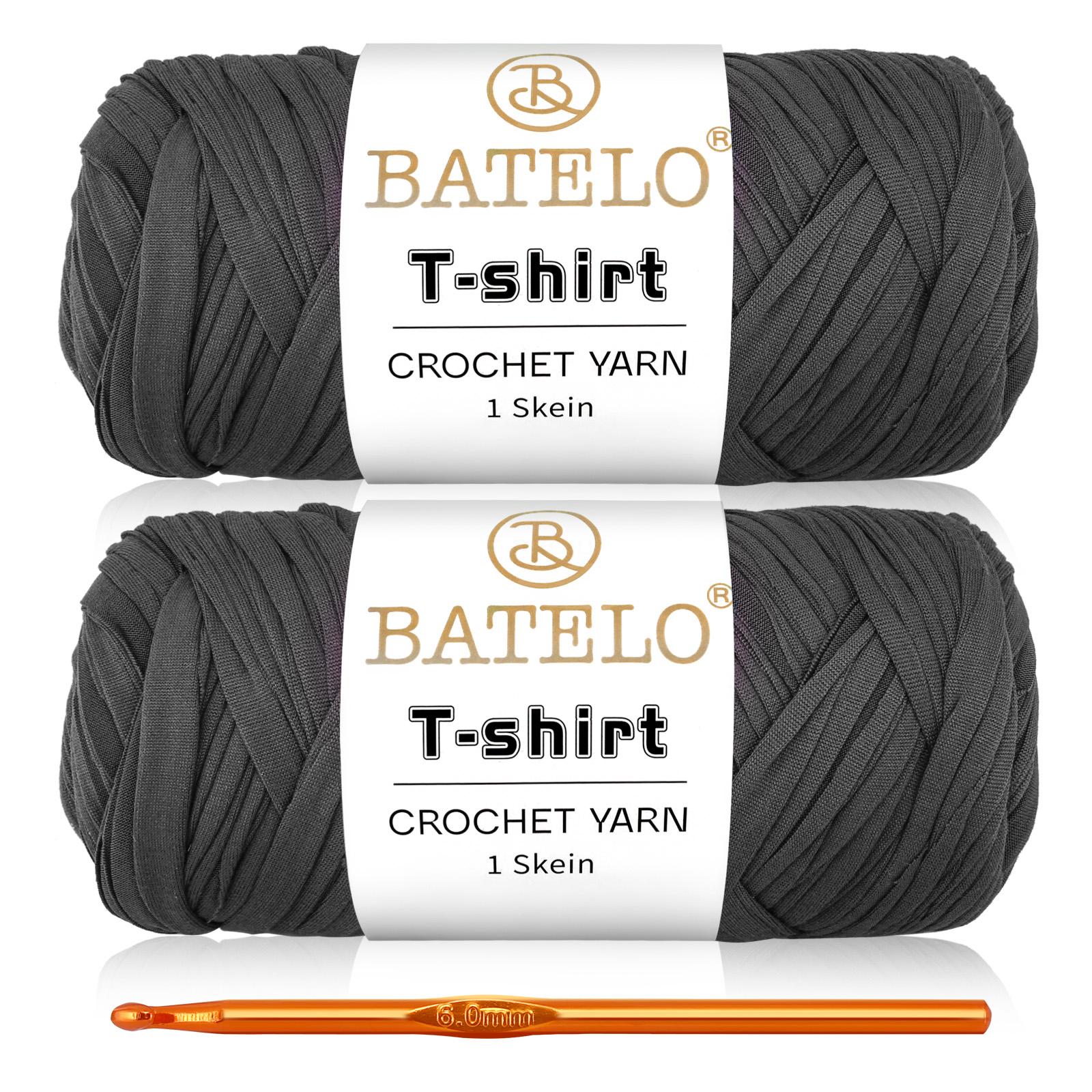 Two charcoal gray BATELO T-shirt yarn skeins with a gold crochet hook on a white background