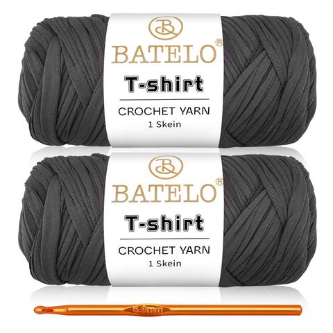 Two charcoal gray BATELO T-shirt yarn skeins with a gold crochet hook on a white background