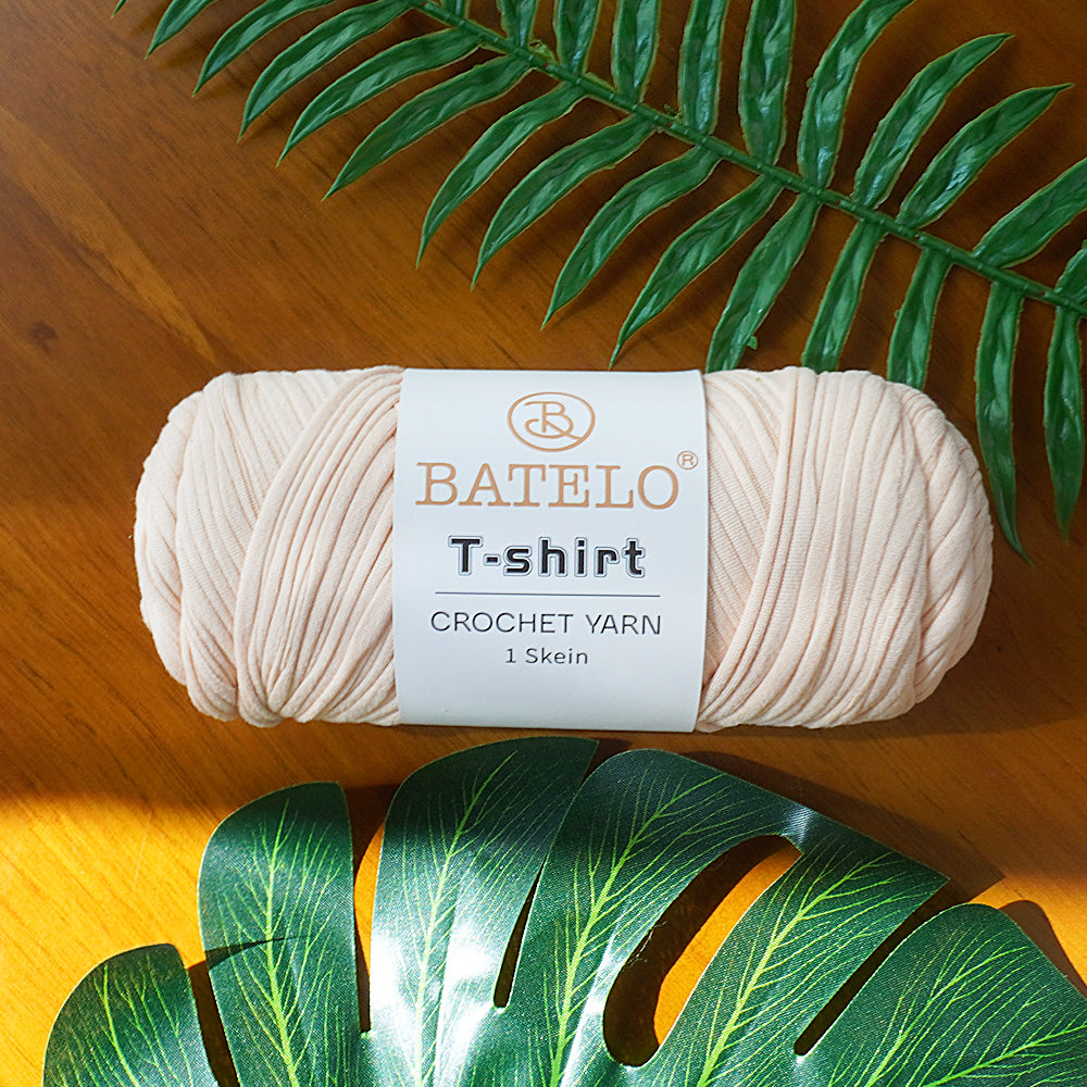 Single cream BATELO T-shirt crochet yarn skein on a wooden table with green leaves