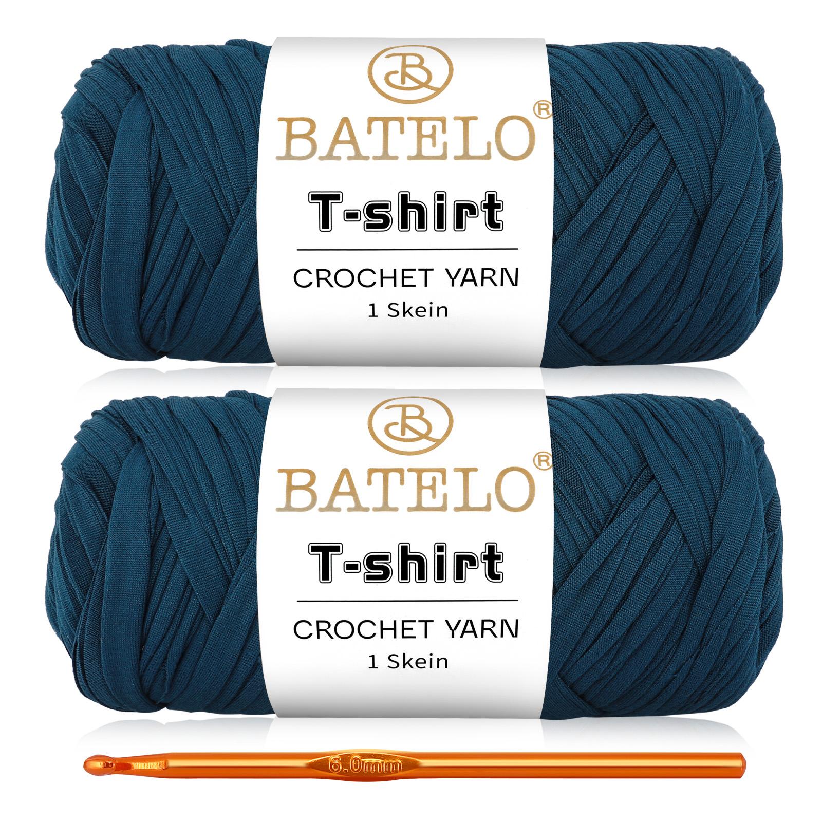 Two dark teal blue BATELO T-shirt yarn skeins with a gold crochet hook on a white background