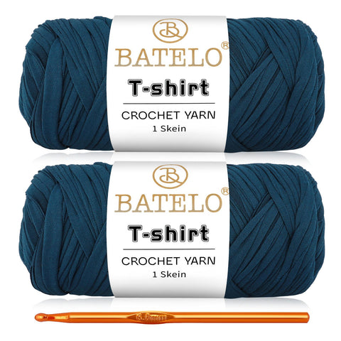 Two dark teal blue BATELO T-shirt yarn skeins with a gold crochet hook on a white background