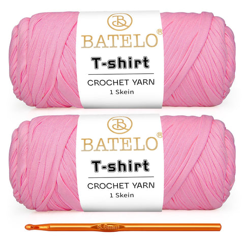 Two soft pink BATELO T-shirt yarn skeins with a gold crochet hook on a white background