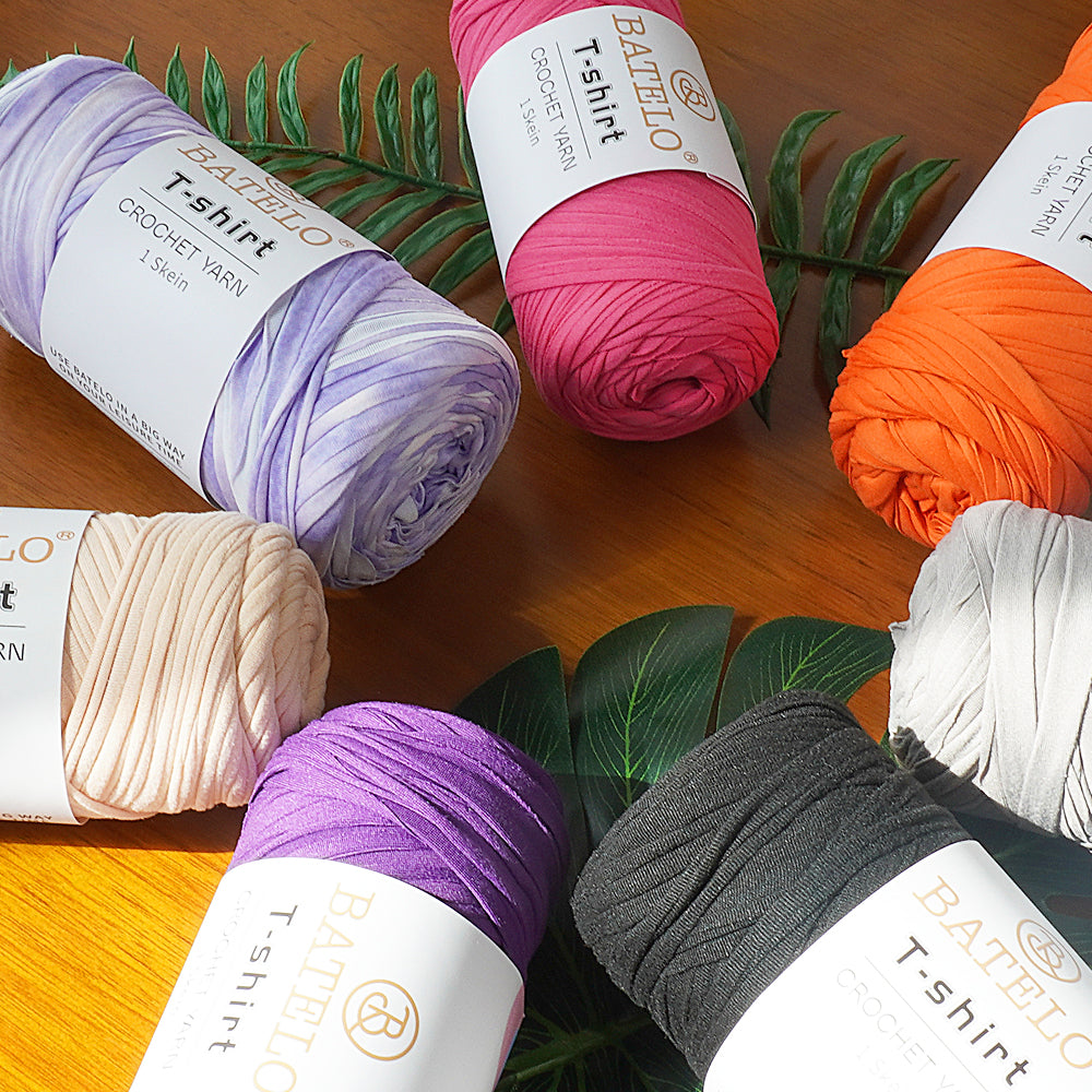Assorted BATELO T-shirt yarn skeins arranged with green leaves on a wooden table