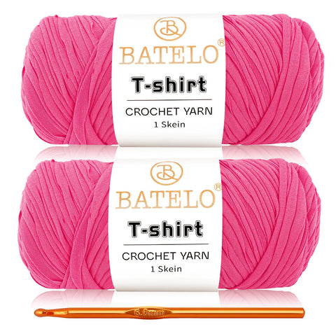 Two hot pink BATELO T-shirt yarn skeins with a gold crochet hook on a white background