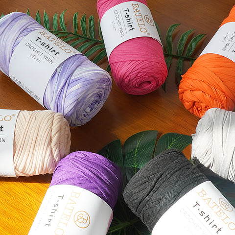 Assorted BATELO T-shirt yarn skeins arranged with green leaves on a wooden table