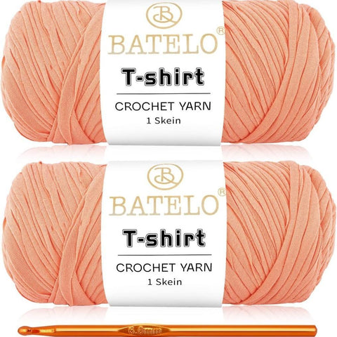 Two peach BATELO T-shirt yarn skeins with a gold crochet hook on a white background