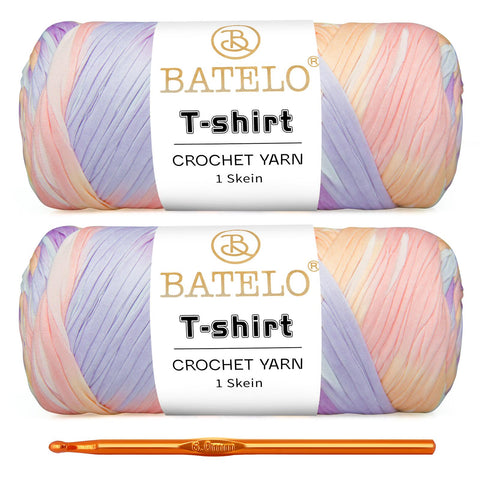 Two pastel pink, lavender, and peach variegated BATELO T-shirt yarn skeins with a gold crochet hook on a white background