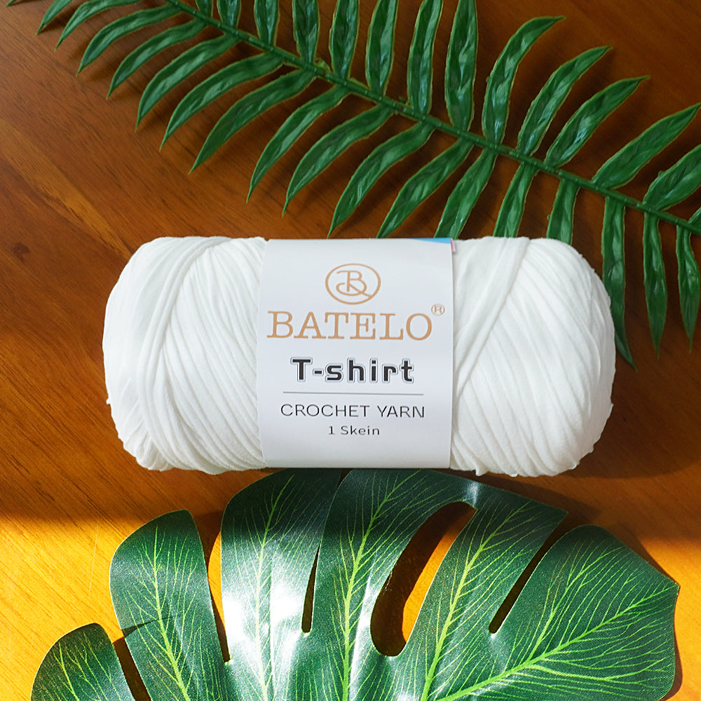 Single white BATELO T-shirt crochet yarn skein on a wooden table with green leaves